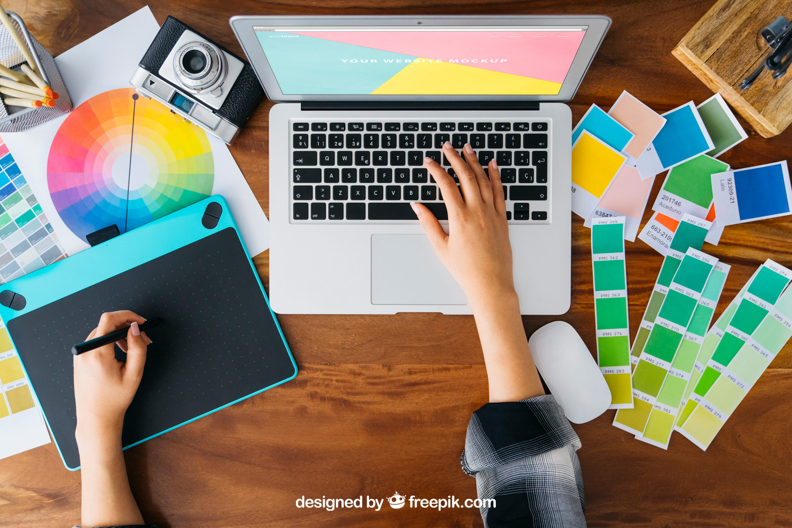 Graphic design creating mock up on laptop with colour schemes on desk.
