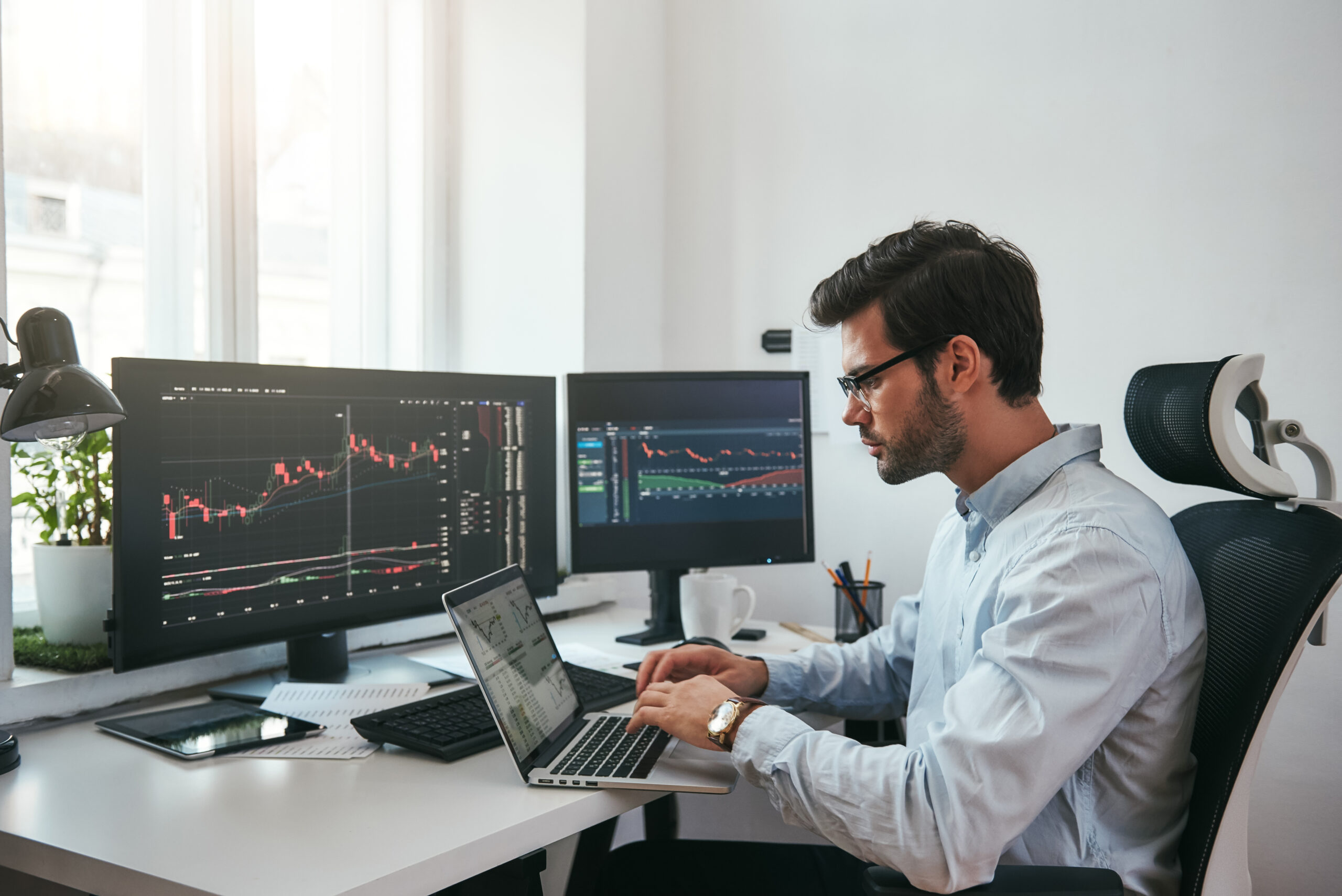Young stock broker working out the best shares to trade on the stock market on his laptop.
