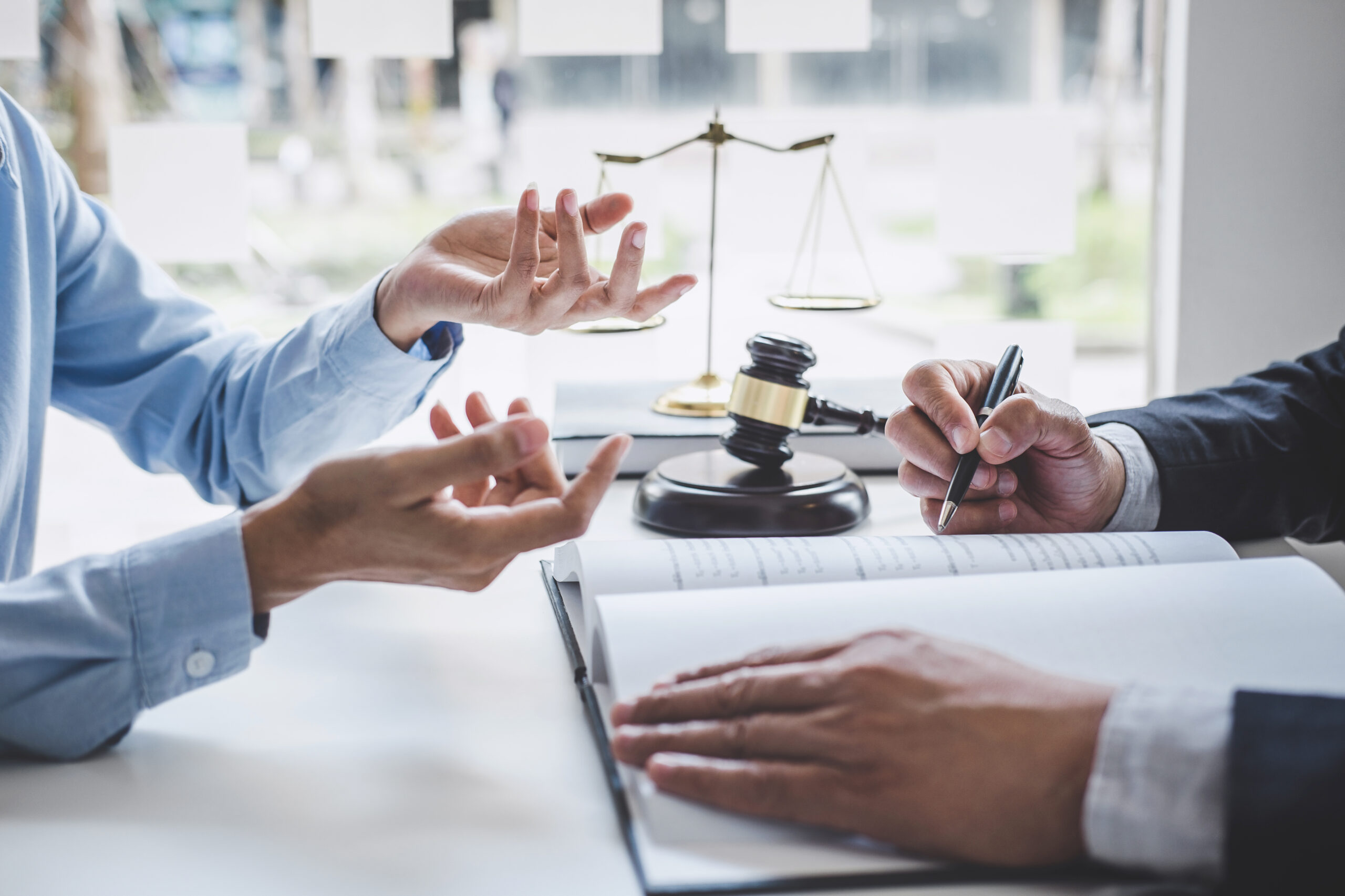 Consultation between lawyer and businesswoman with hammer and scales on desk in background