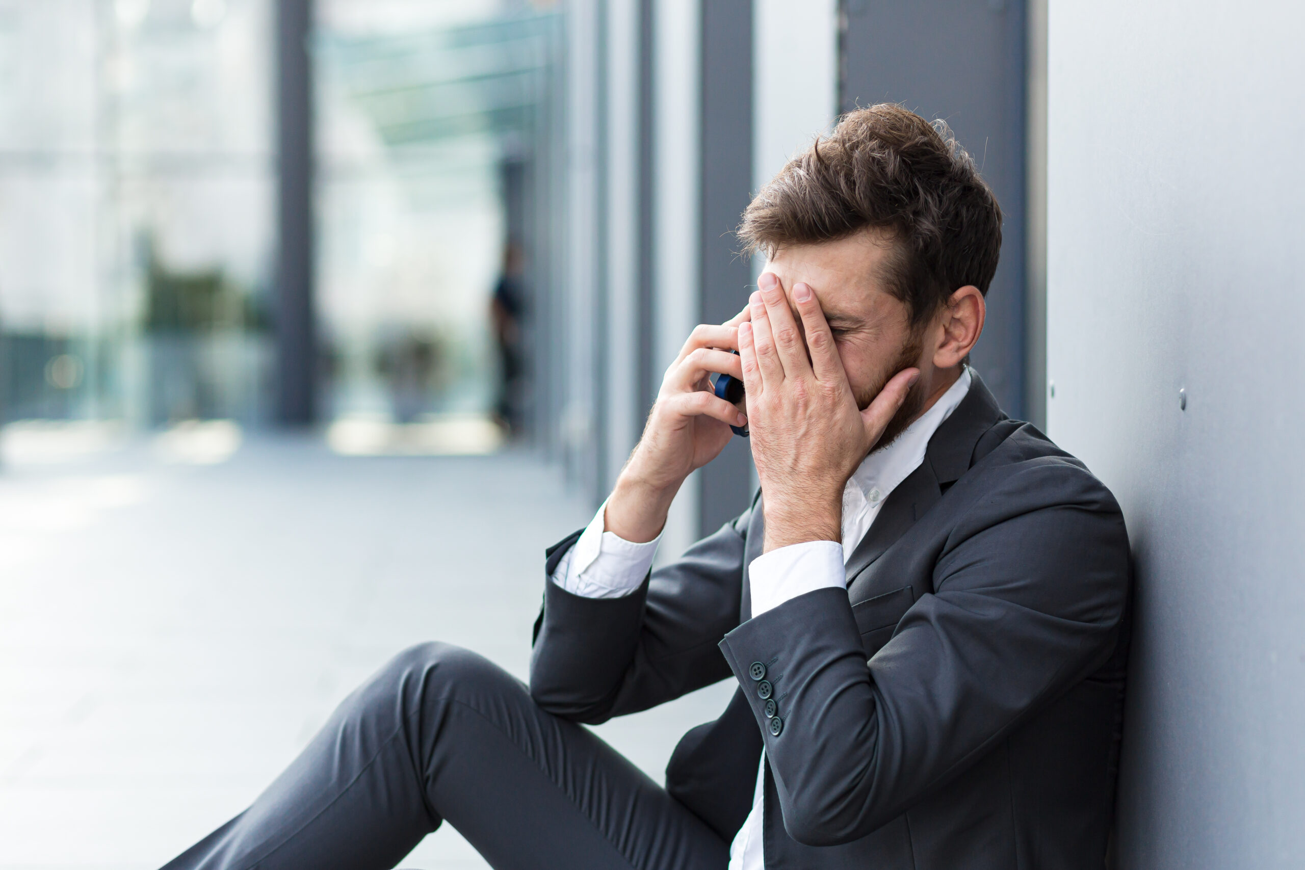 Depressed office worker struggling with mental health on the phone outside of office building