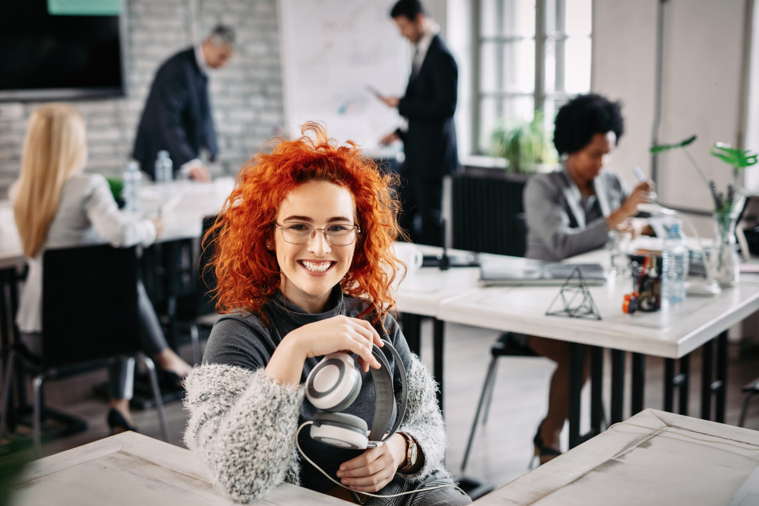 Happy redhead businesswoman with headphones sitting in the office.