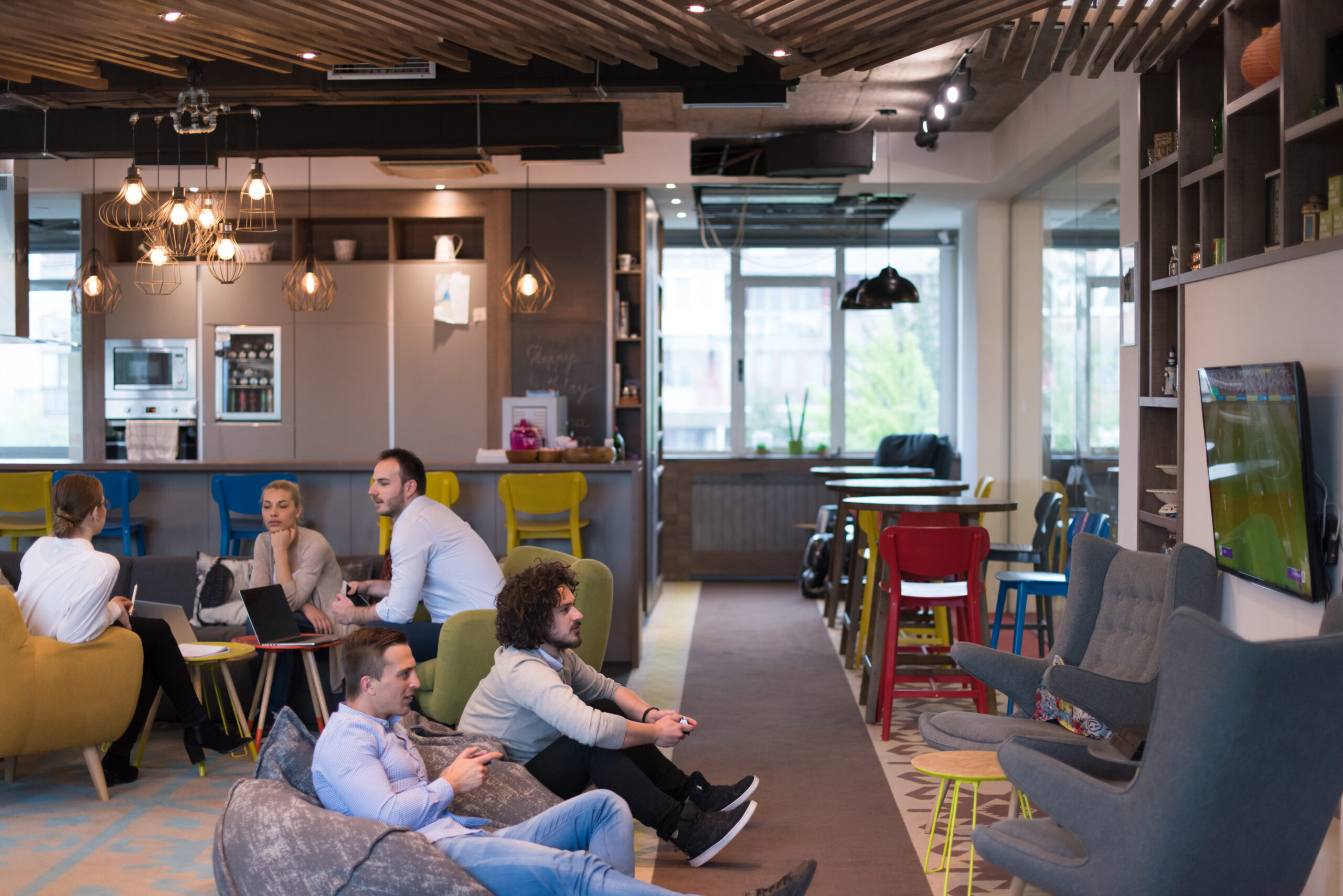 Startup office breakout area, with employees playing video games and sitting round a table