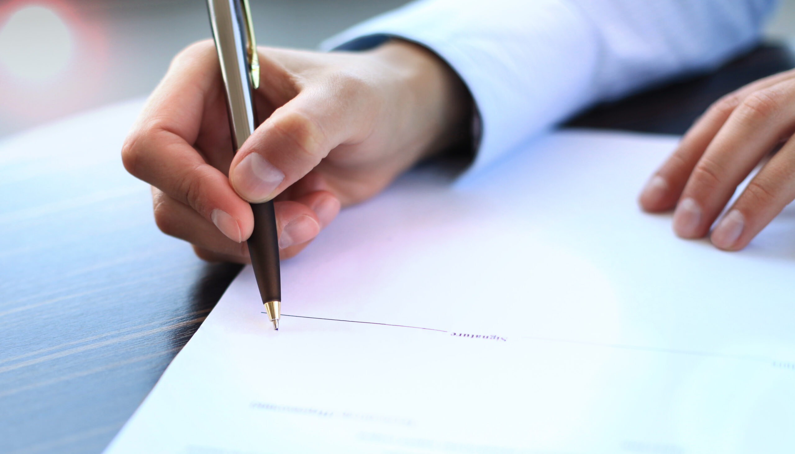 Businesswoman sitting at office desk signing a contract with shallow focus on signature.